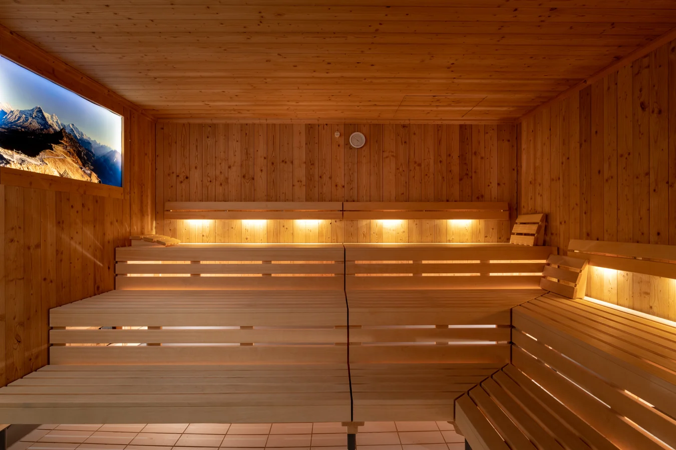 The sauna at Victoria Lauberhorn in Wengen, with tiered wooden benches, wood-panelled walls and warm recessed lighting