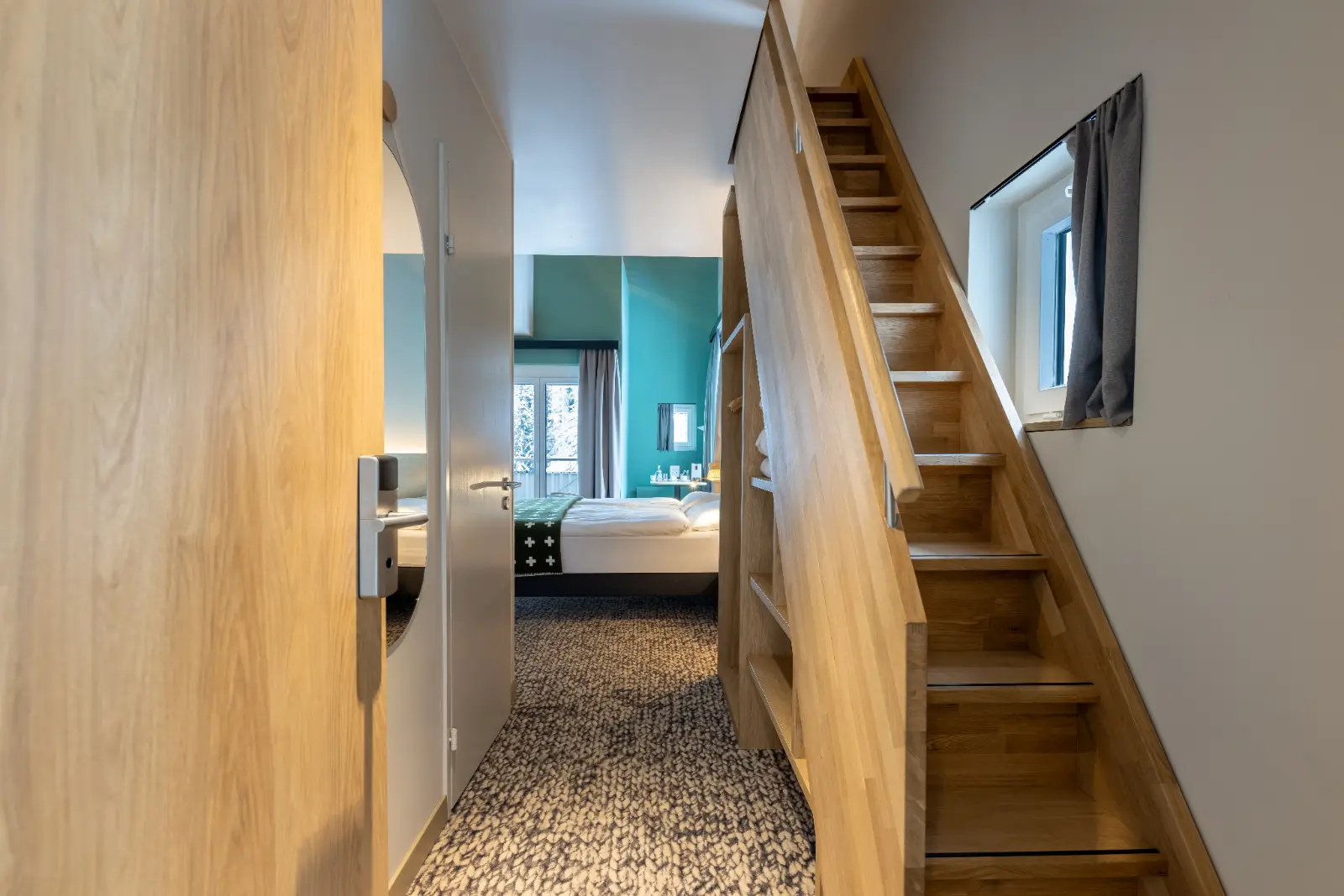 View into a bedroom with wooden stairs, carpeted floor, turquoise wall, and a bed with white linens.