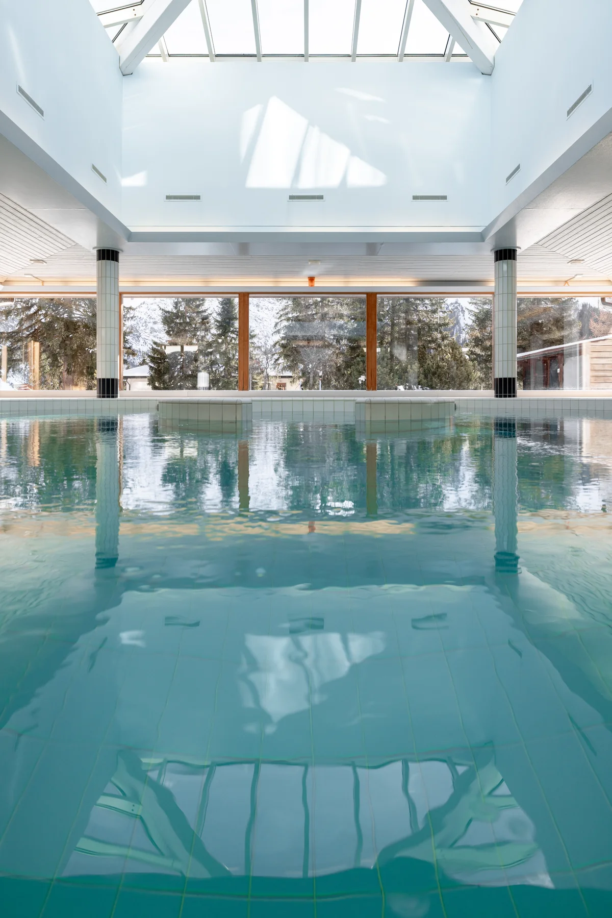 The indoor pool at Altein, Arosa, lit by a long glass skylight, with winter trees outside the windows