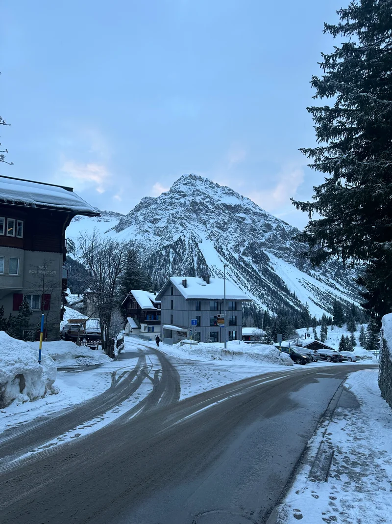 Strada innevata che attraversa Arosa sotto un cielo coperto, con chalet e una vetta innevata sullo sfondo