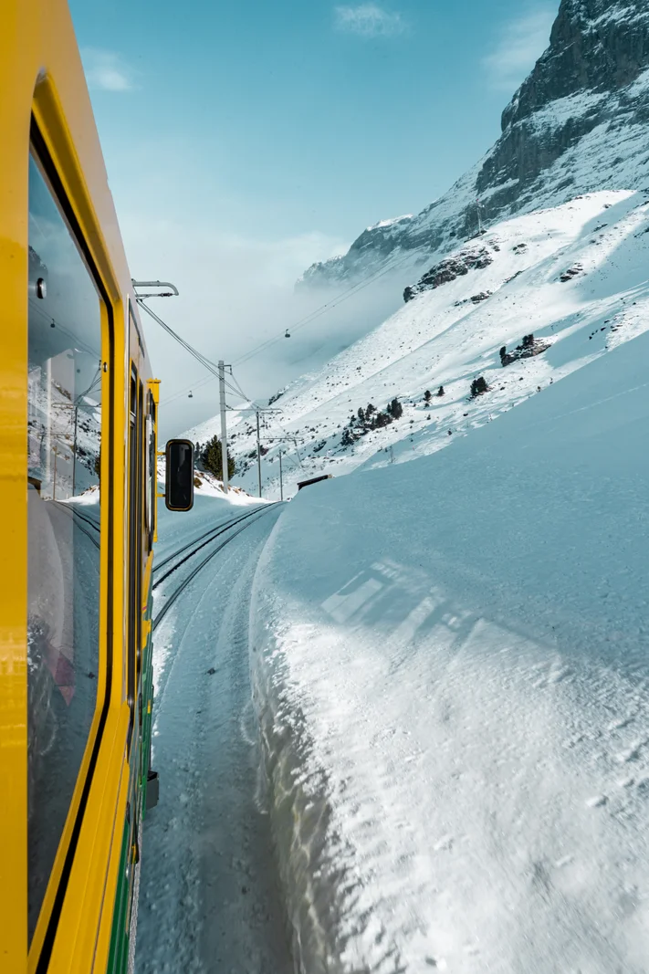 View from the Wengernalpbahn train window along the snowy track, with steep snow-covered slopes above