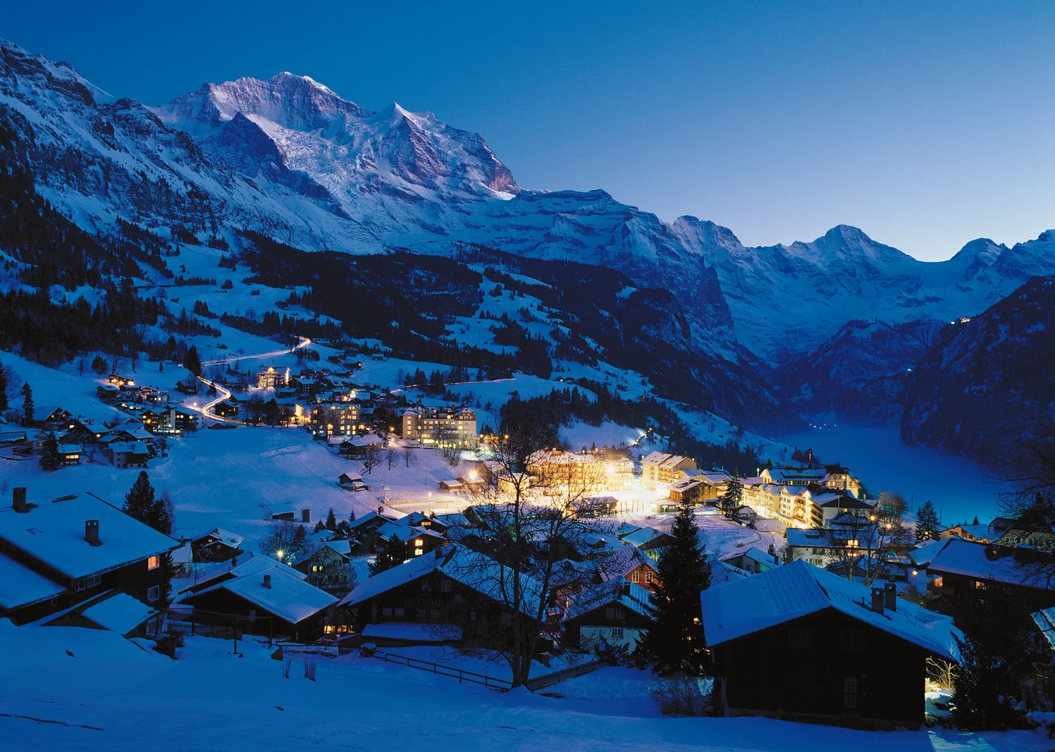 Wengen village lit at night under snow, with the Jungfrau behind