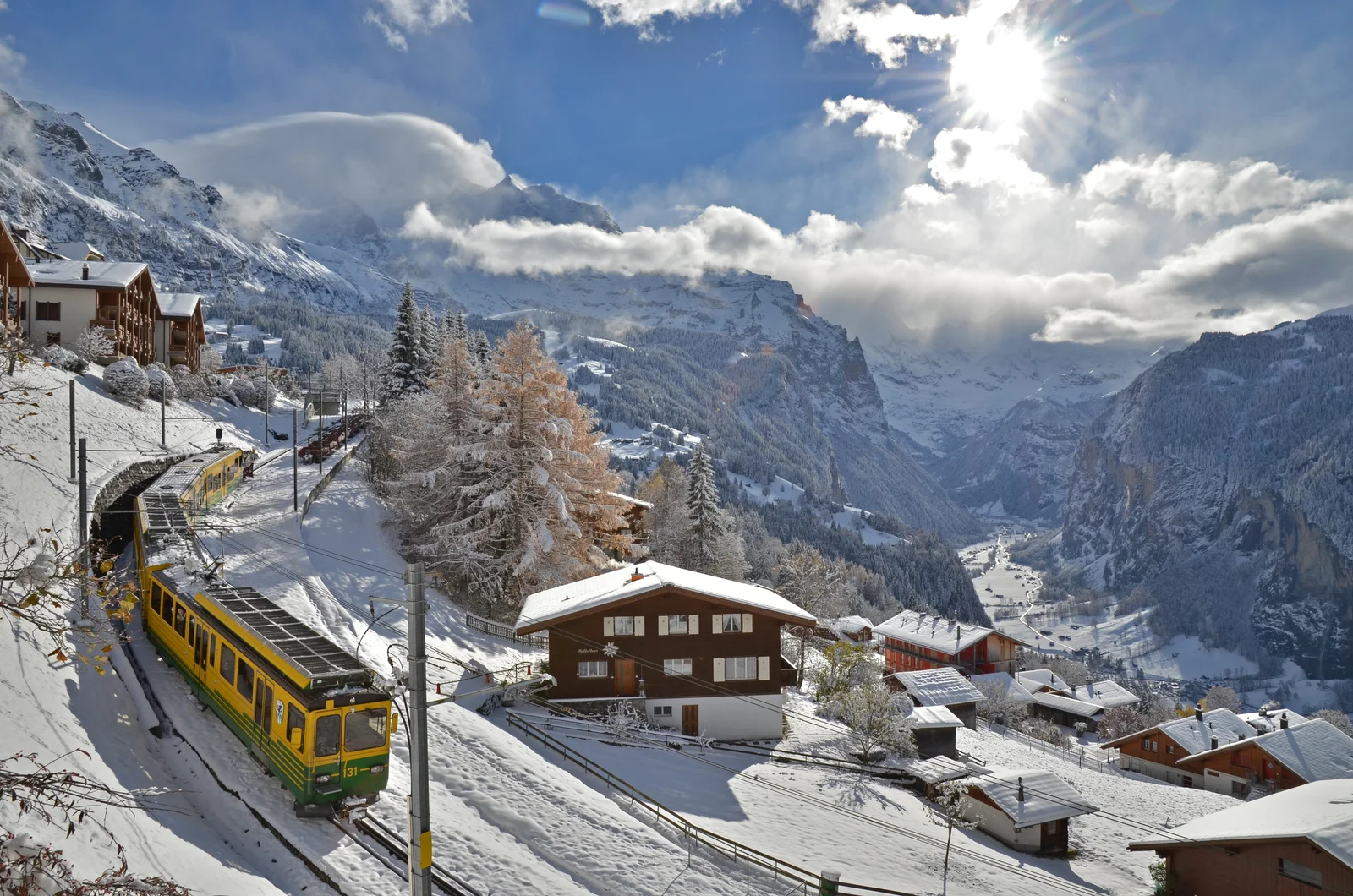 Wengernalpbahn train on the snowy curve above Wengen village, with chalets and the Lauterbrunnen valley below