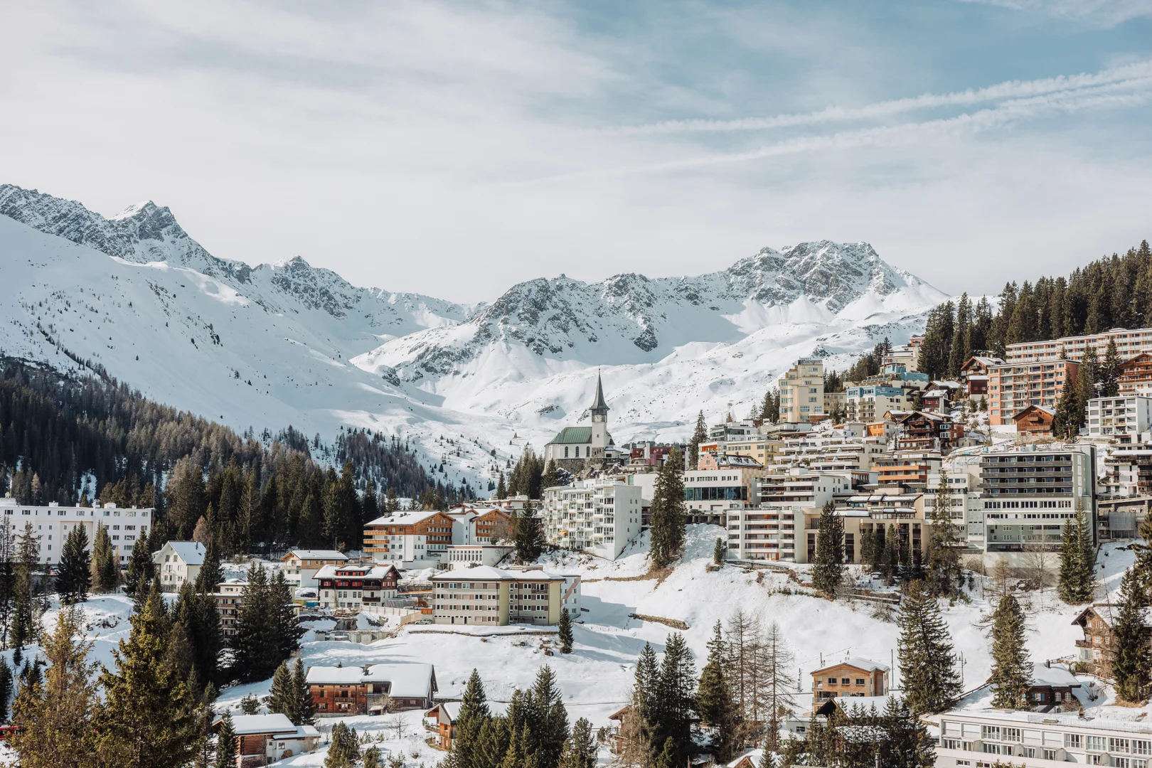 Das Dorf Arosa am verschneiten Hang, mit Kirchturm und verschneiten Gipfeln dahinter