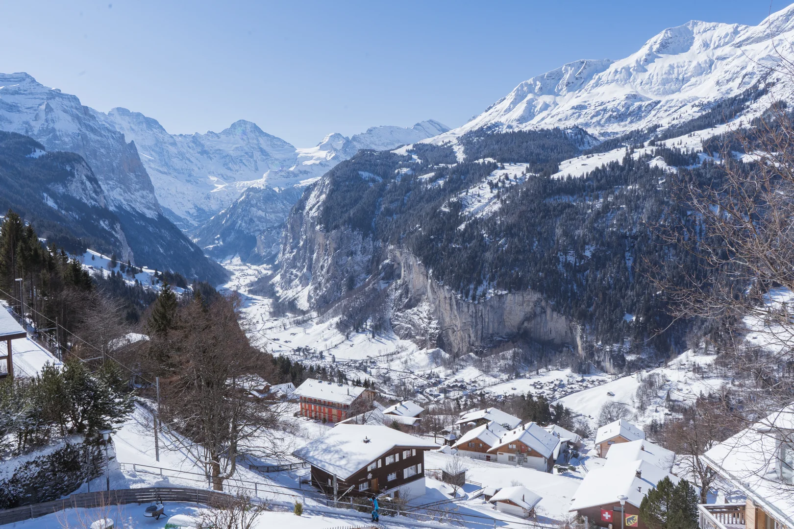 Blick über verschneite Chalets in Wengen hinunter ins Lauterbrunnental mit seinen Felswänden und Gipfeln