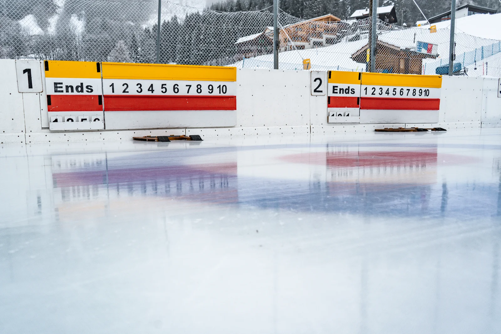 Curlingbahn im Freien mit Anzeigetafeln an der Eisbahn Wengen, dahinter verschneite Chalets