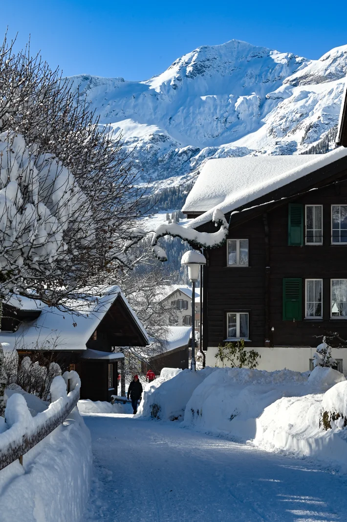 Geräumter Weg zwischen verschneiten Chalets in Wengen, dahinter die Jungfrau