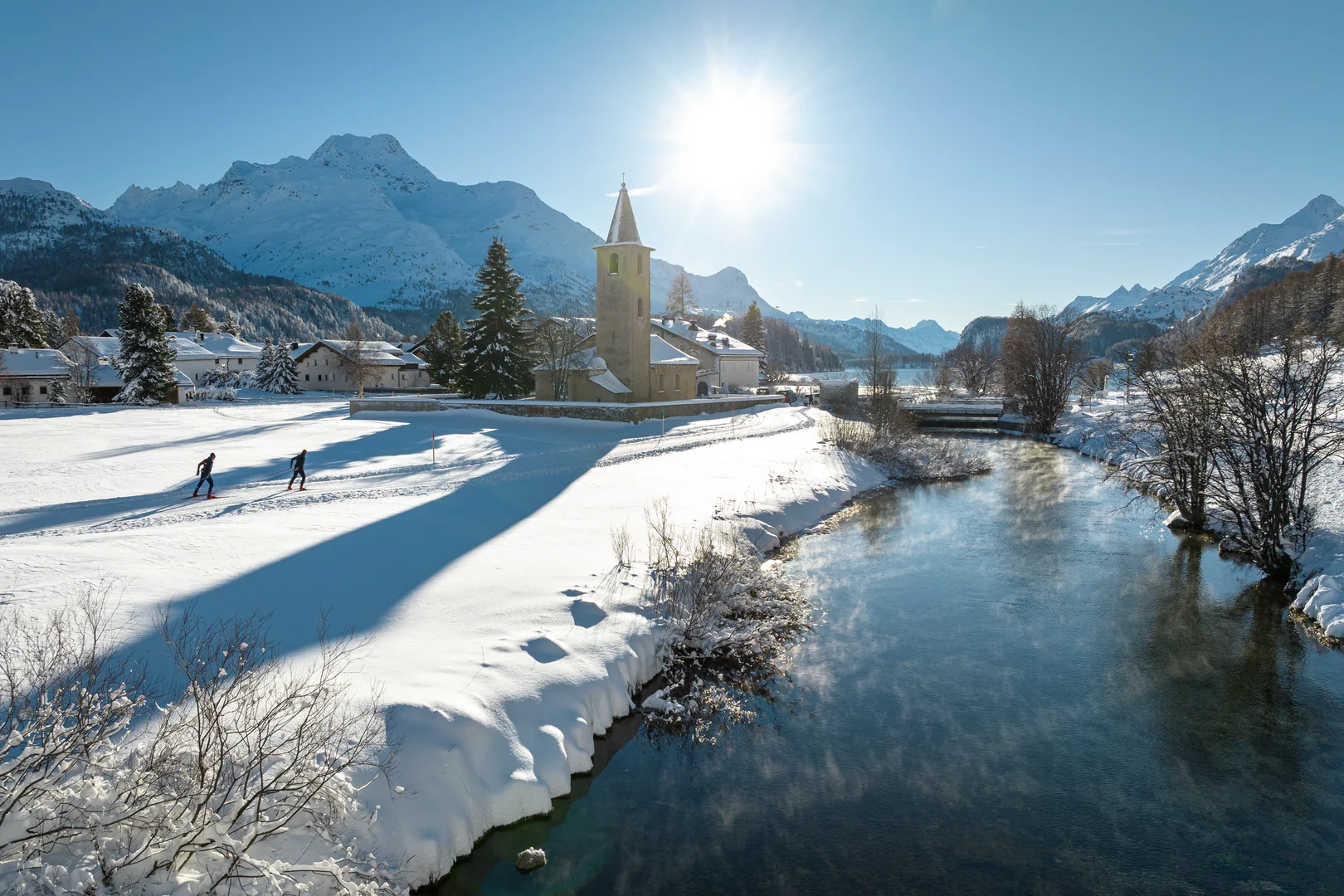 Fondisti sulla pista battuta della piana di Sils con la chiesa di Sils Baselgia e le cime innevate alle spalle