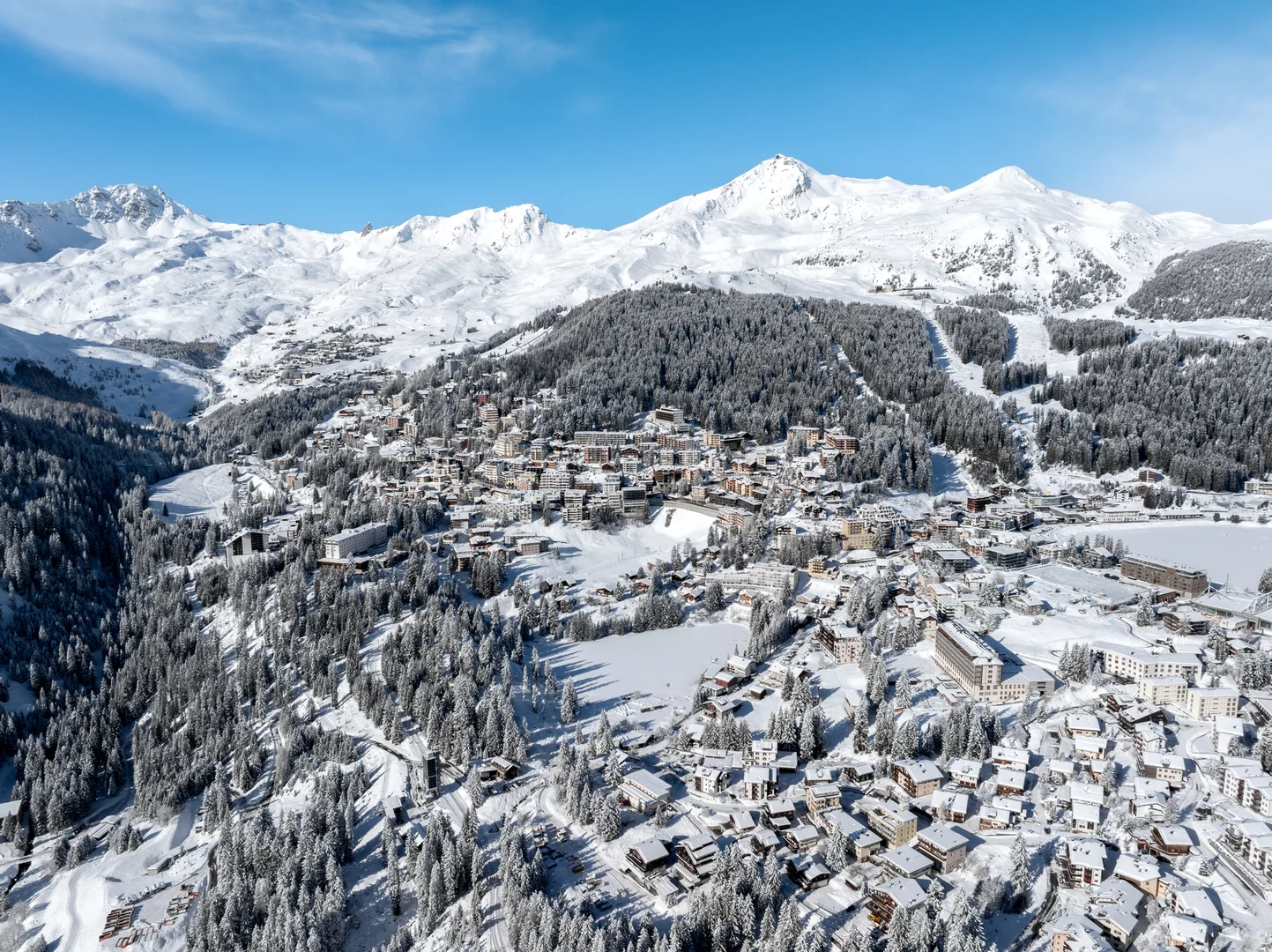 Aerial view of Arosa in snow, the village spread across forested slopes below white peaks