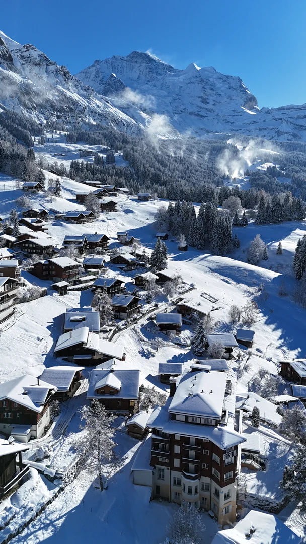 Luftaufnahme des verschneiten Wengen auf seiner Terrasse, dahinter die Jungfrau
