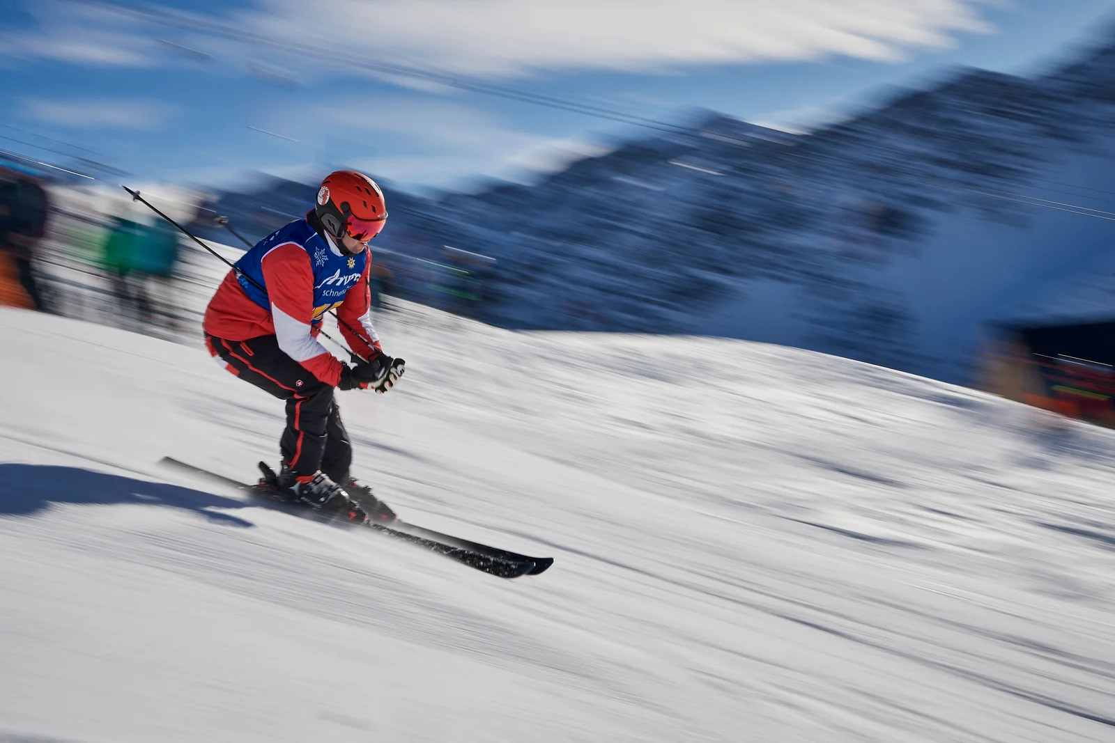 Sciatore da gara con casco rosso e pettorale lanciato su una pista battuta in una giornata di sole
