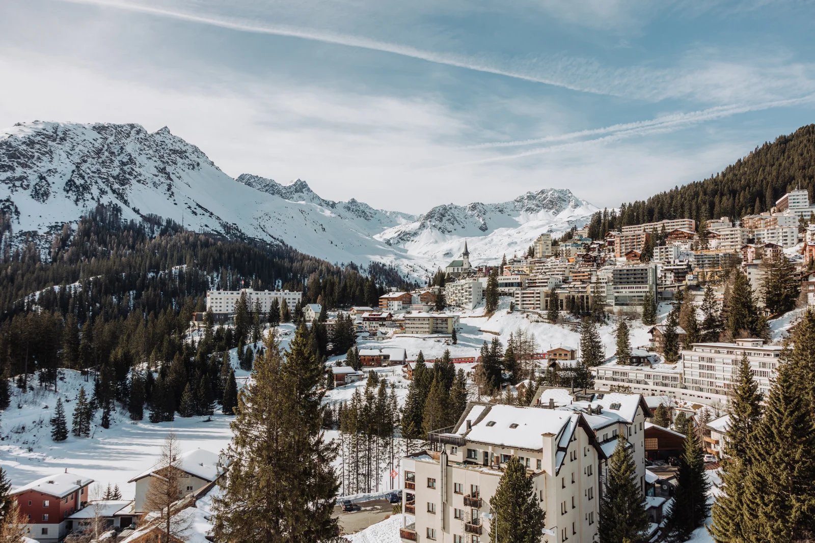 Arosa sul pendio innevato, abeti e un hotel in primo piano, cime innevate a sinistra