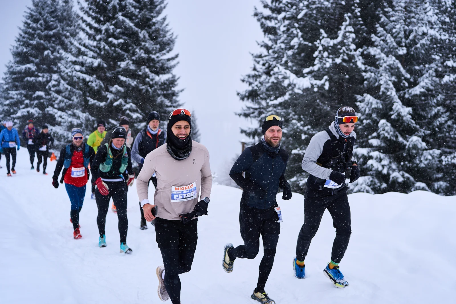 Runners on a snow-covered forest path between snow-laden firs during the Snow Walk and Run in Arosa
