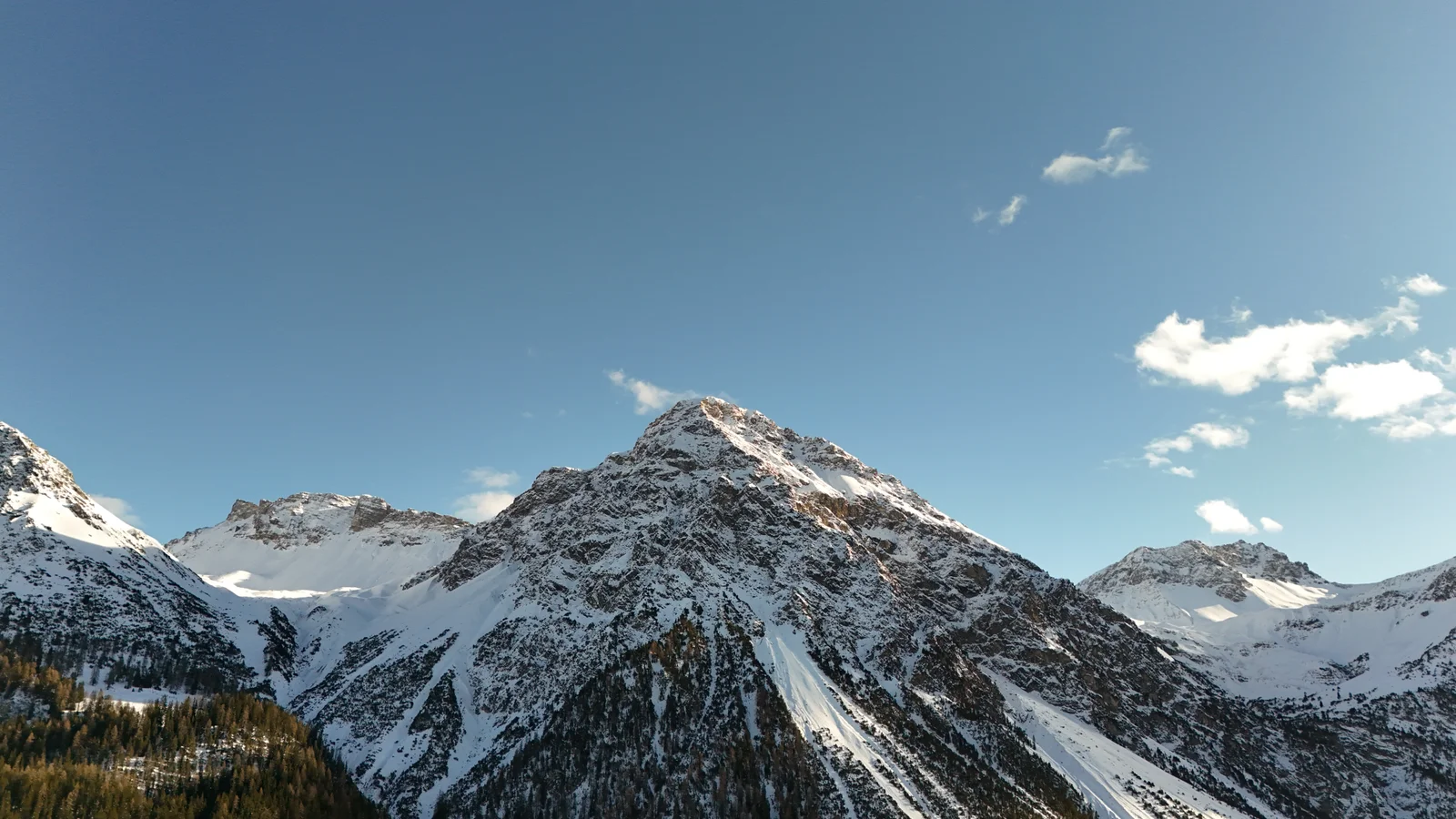 Snow-covered rocky peaks above a dark evergreen forest near Arosa under a clear sky