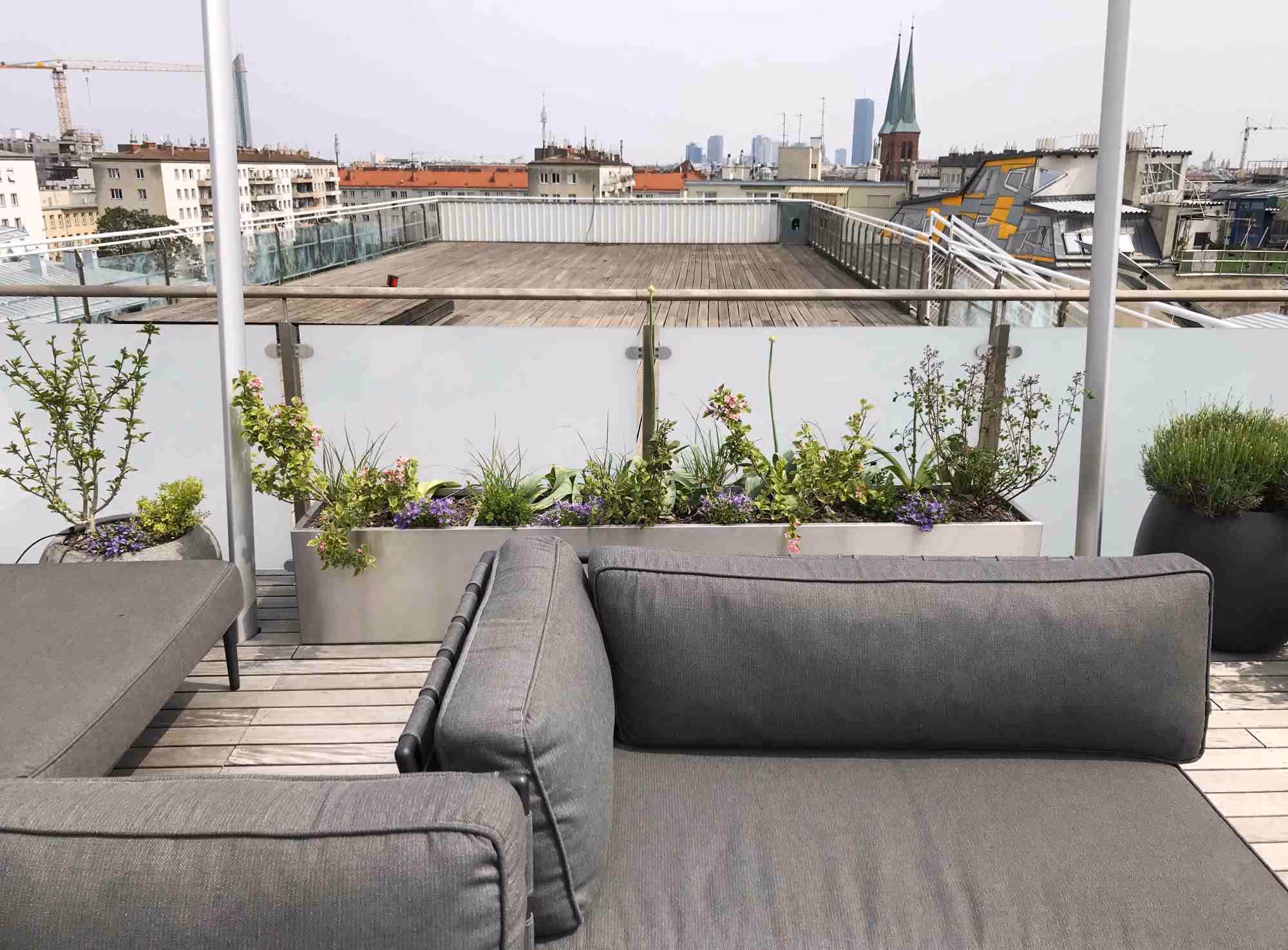 Moderne Rooftop-Terrasse mit grauer Outdoor-Sitzlounge und maßgefertigten Pflanztrögen.