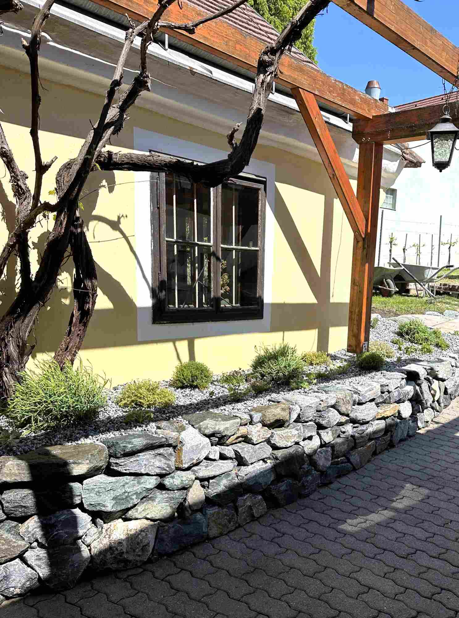 Gartenweg entlang eines Hauses mit heller Natursteinmauer