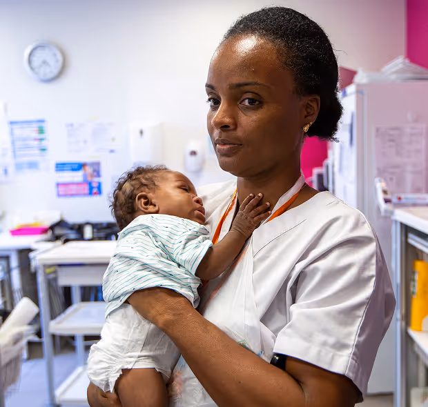 A nurse gently holds a sleeping baby in a clinic setting.
