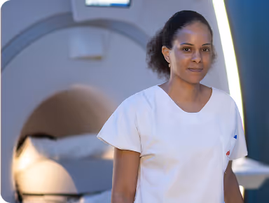 A woman in a white medical uniform stands near a medical imaging machine.