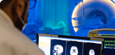 A person observes brain scans on a computer screen next to an active MRI machine.
