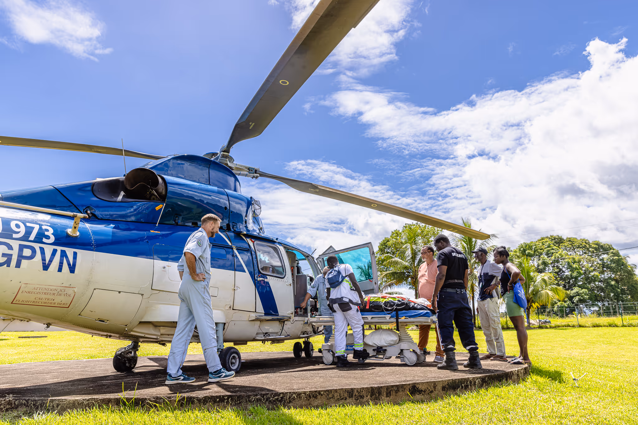 Medical team loads a stretcher into a helicopter while others stand nearby on a sunny day.