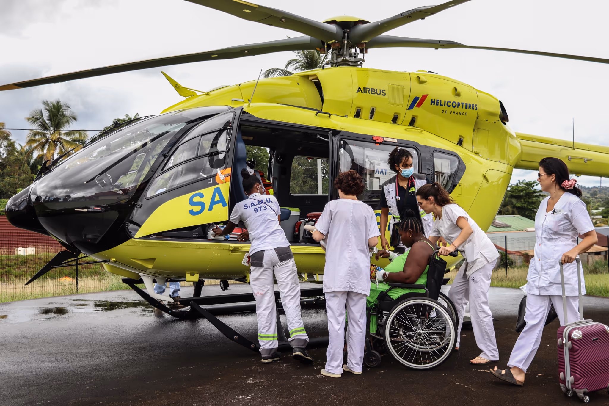 Medical team assists a patient from a wheelchair into a yellow rescue helicopter.