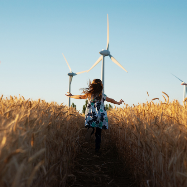 Girl running through field and wind turbine in the background