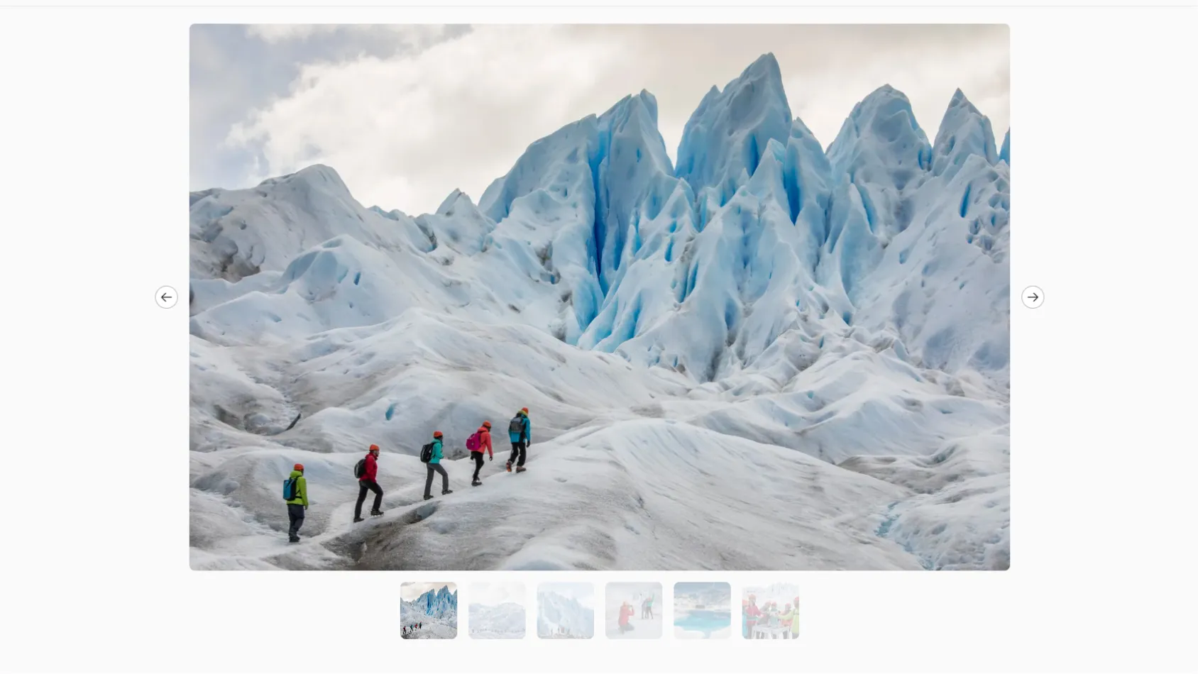 Group of hikers walking in single file on a glacier with towering blue ice formations.