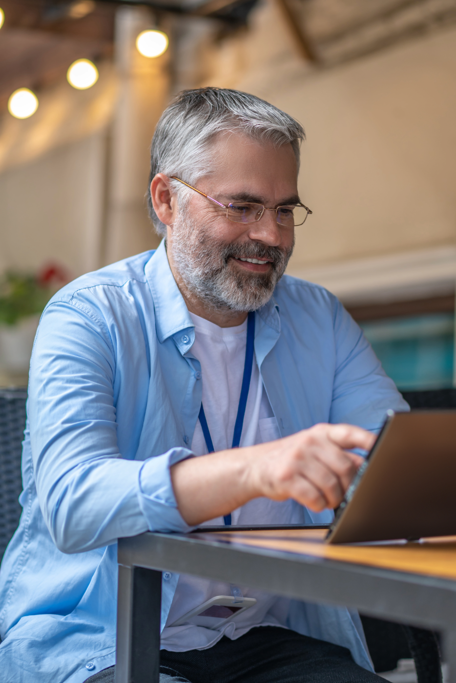 Woman with glasses sitting barefoot on a gray sofa using a laptop in a cozy modern living room with wooden stairs and light decor.