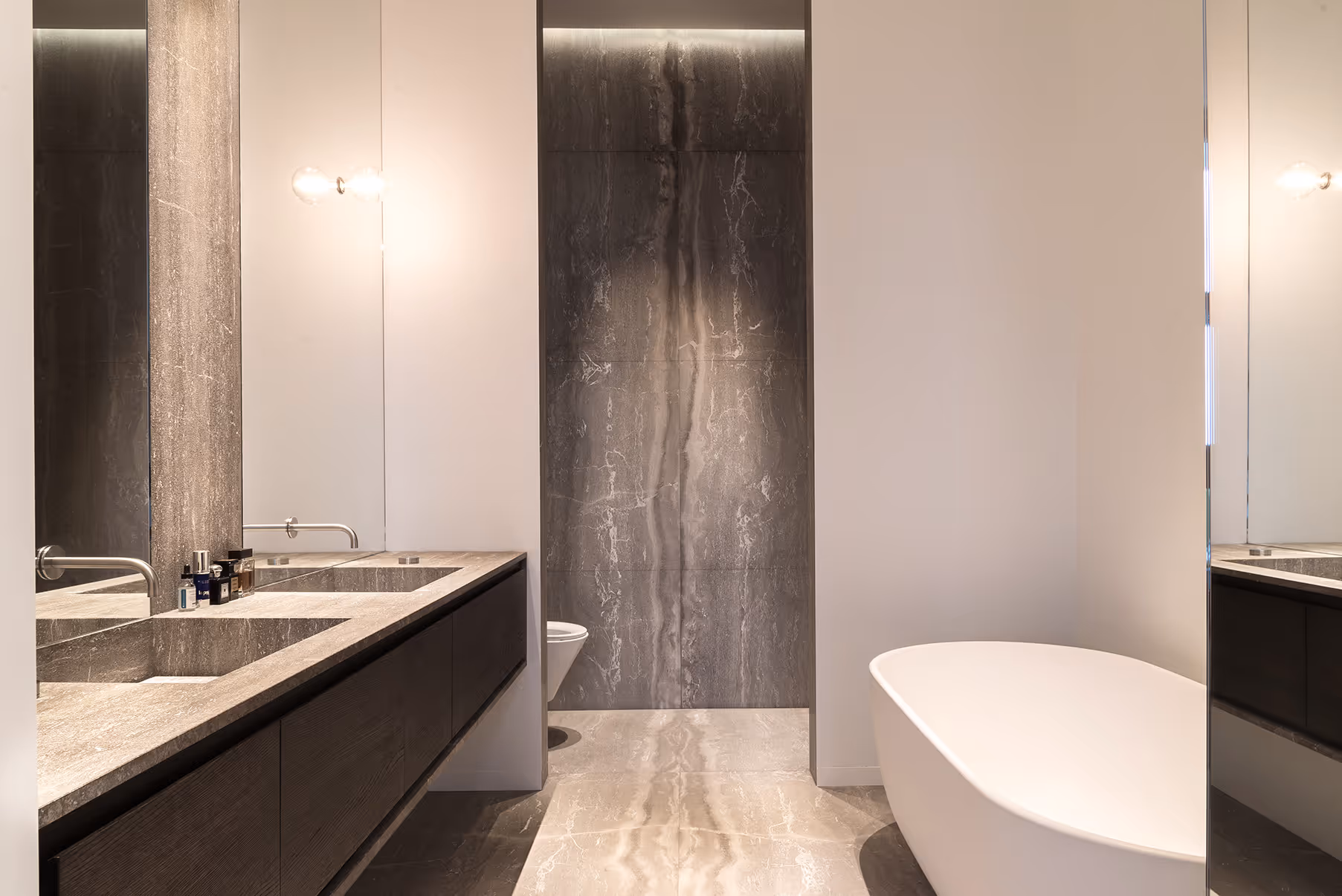 Modern bathroom with double stone sinks, wall-mounted faucets, freestanding white bathtub, and gray marble accents.