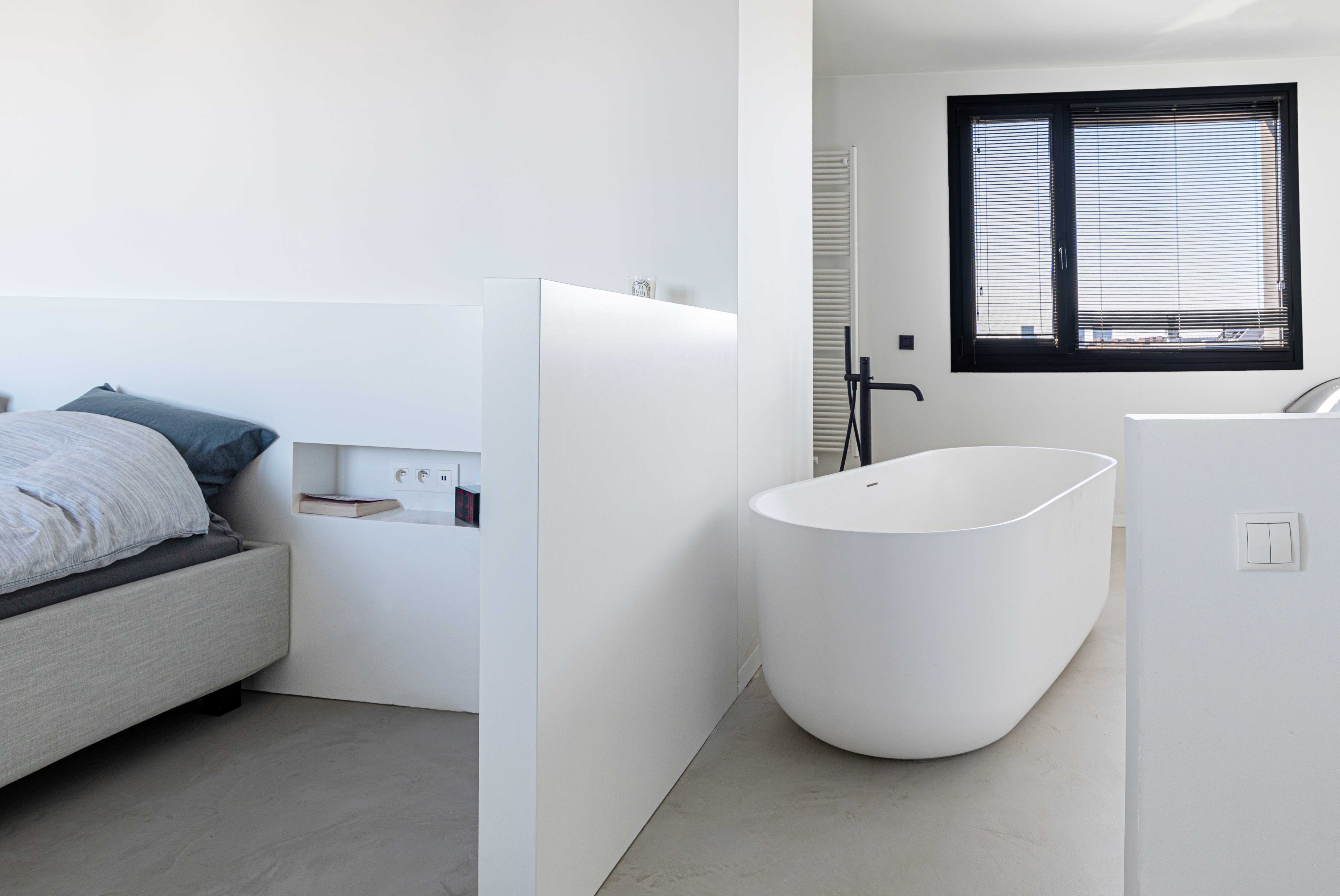 Bright room with three tall windows, light curtains, wooden floor, black swivel chair with blue blanket, TV on wooden stand, and a shelving unit with basketball and books.