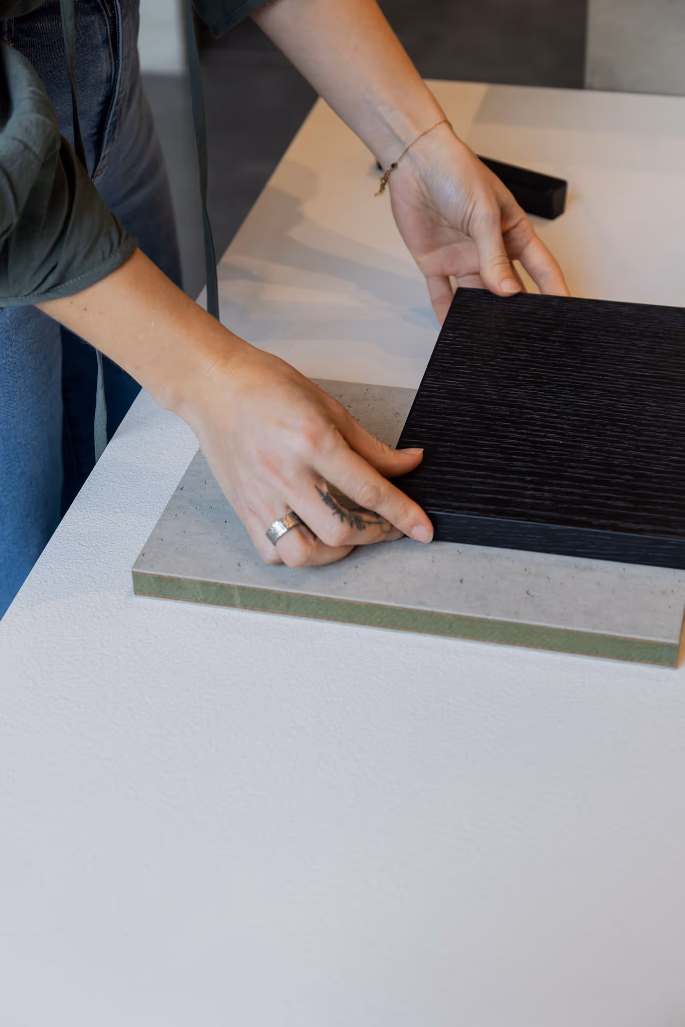 Person's hands placing a dark wood textured sample on top of a gray stone textured sample on a white table.
