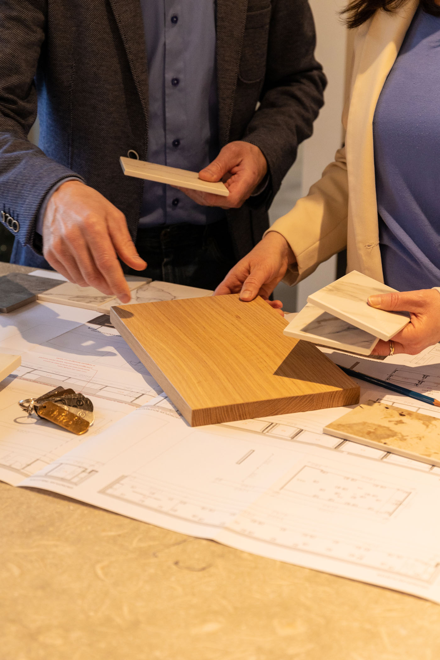 Two people discussing and comparing wooden and marble tile samples over architectural blueprints.