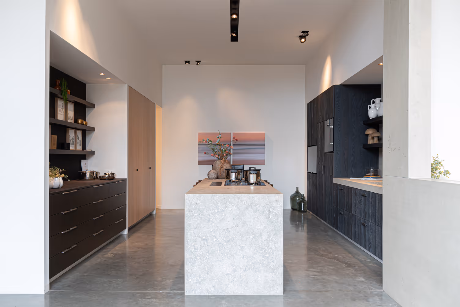 Minimalist modern kitchen with a central marble island, dark cabinets, and decorative vases and plants.