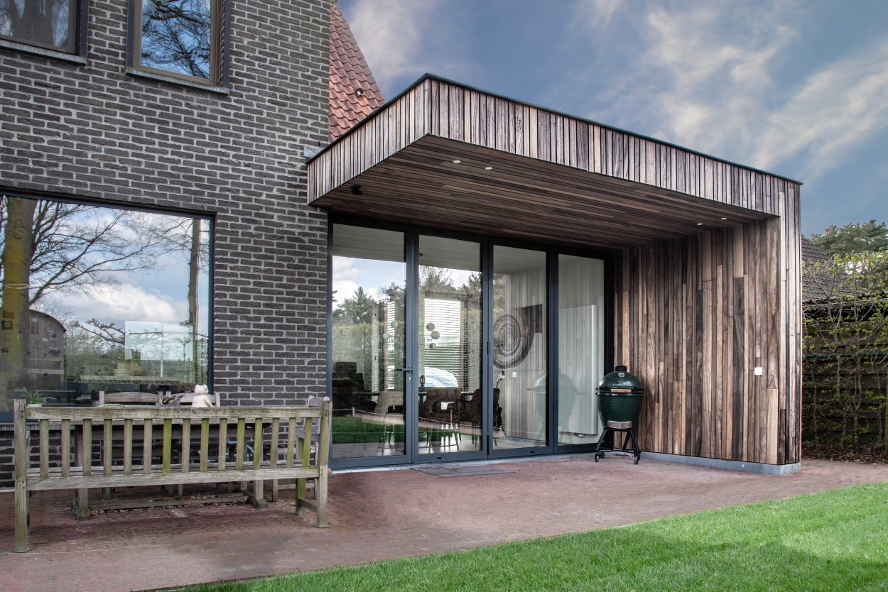 Modern interior with vertical wooden wall panels, a large glass window with blinds, and a guitar resting on the floor inside.