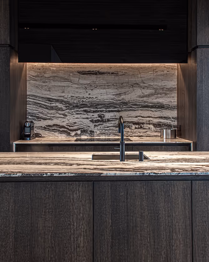 Detail van een moderne keuken met marmeren spatwand, zwarte kraan en donkere houtaccenten.
