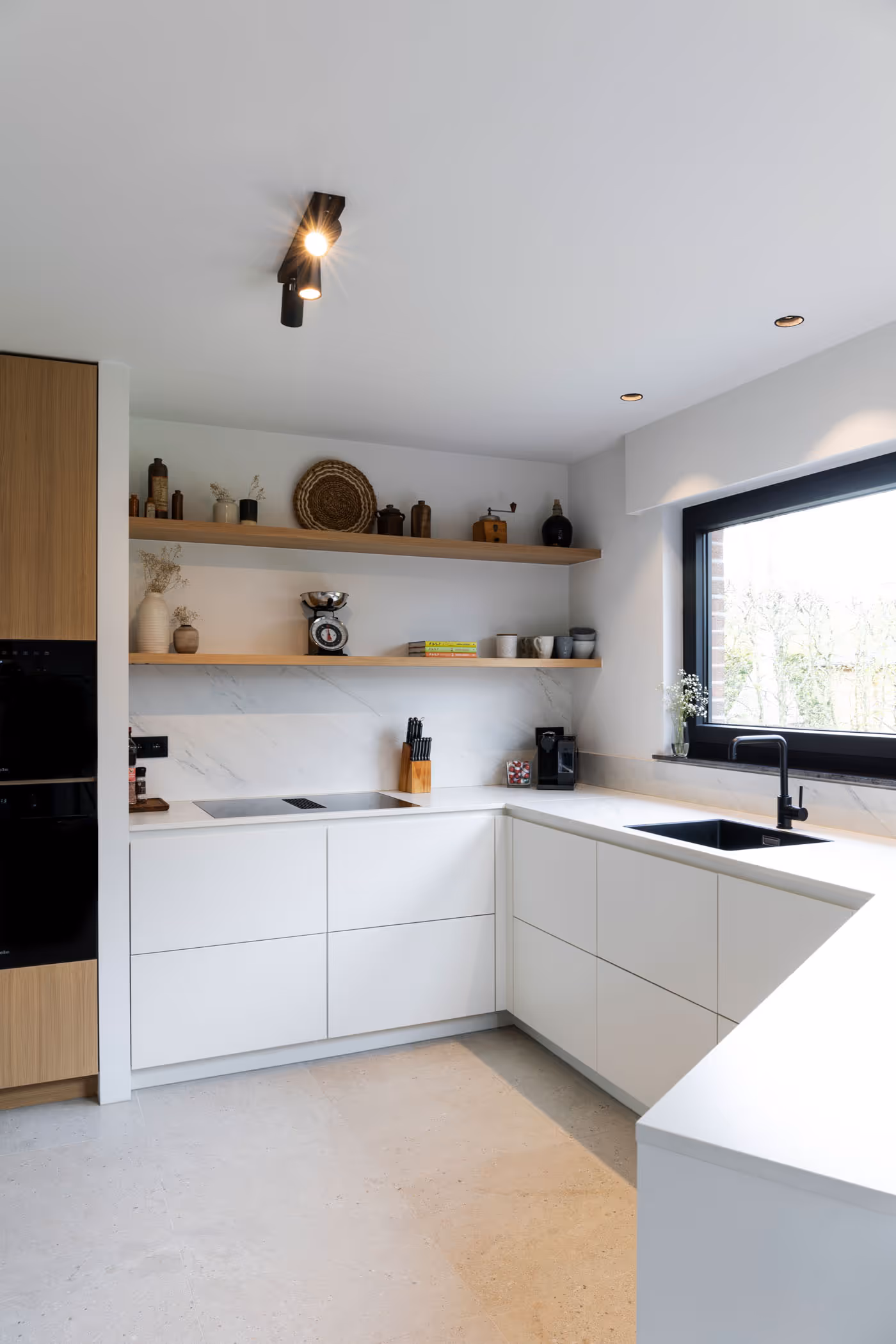 L-vormige keuken met witte kasten, zwarte spoelbak en houten open planken tegen een marmerlook spatwand.