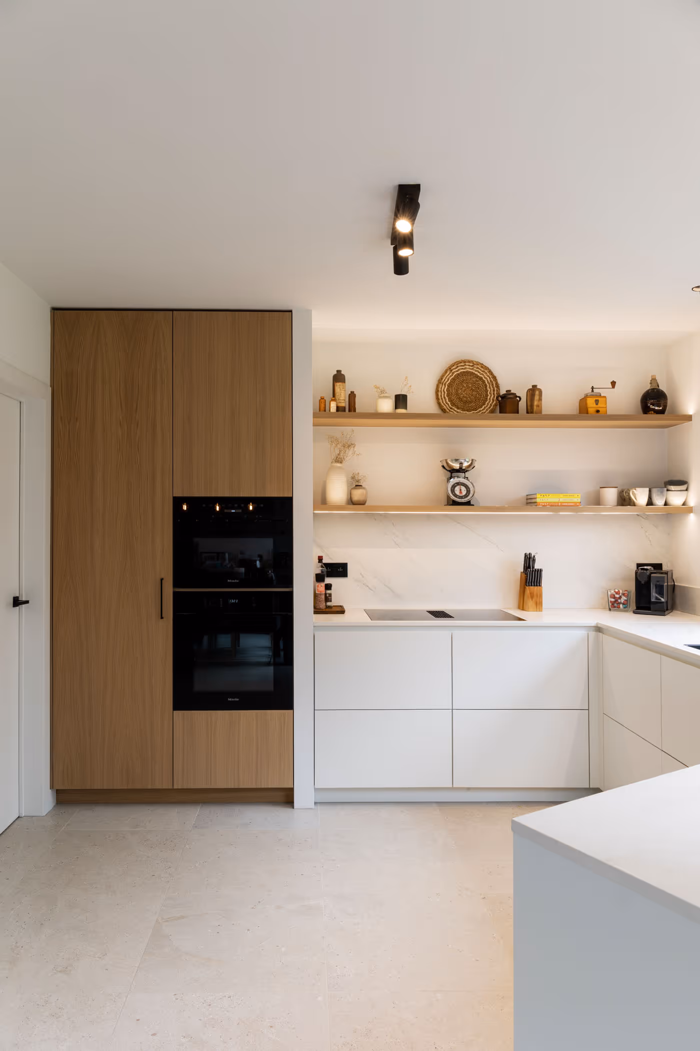 Strakke witte keuken met zwarte ramen, houten kastenwand en decoratieve open legplanken met aardse accessoires.