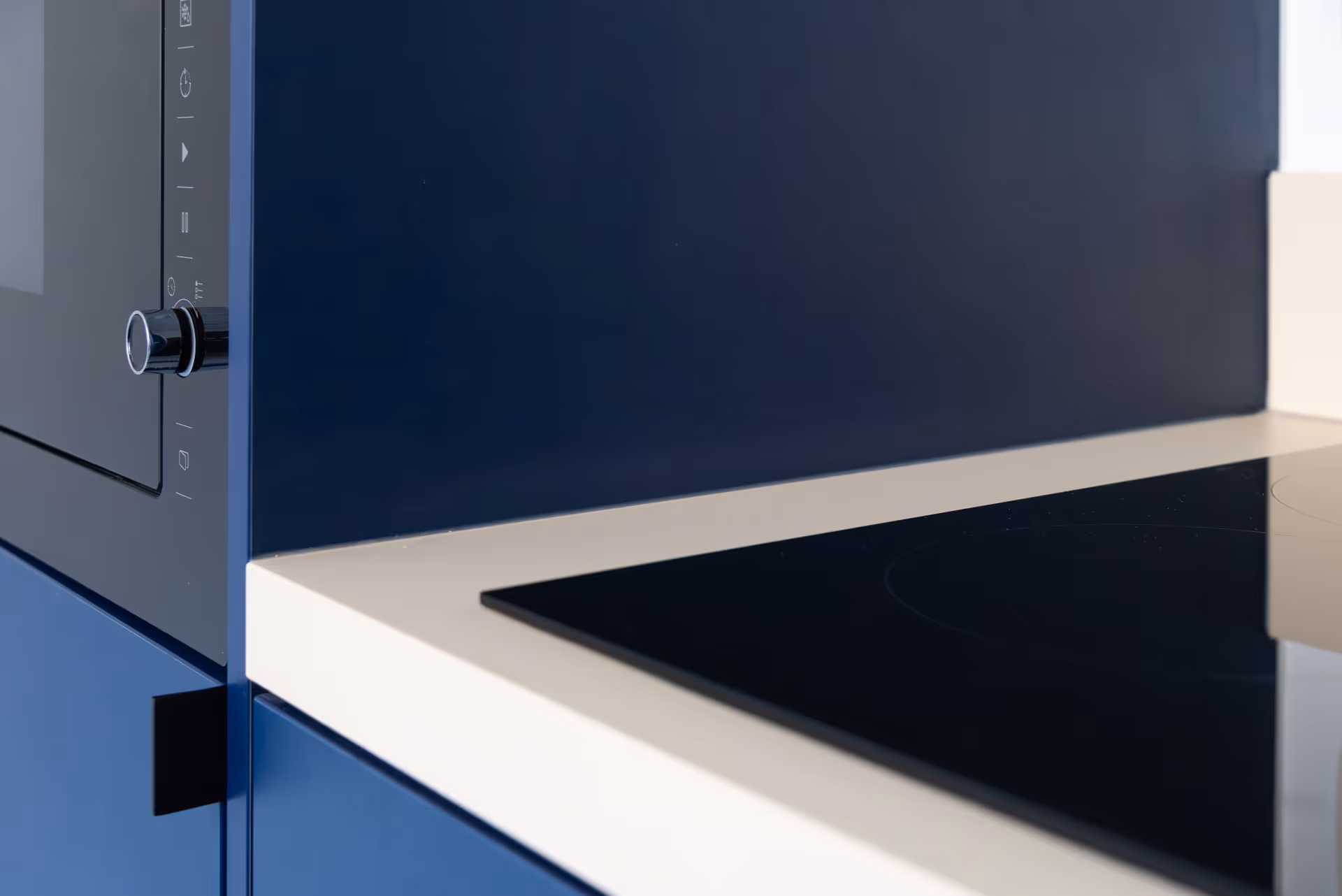 Close-up van een moderne inductiekookplaat en ingebouwde oven in een blauwe keuken met licht werkblad.