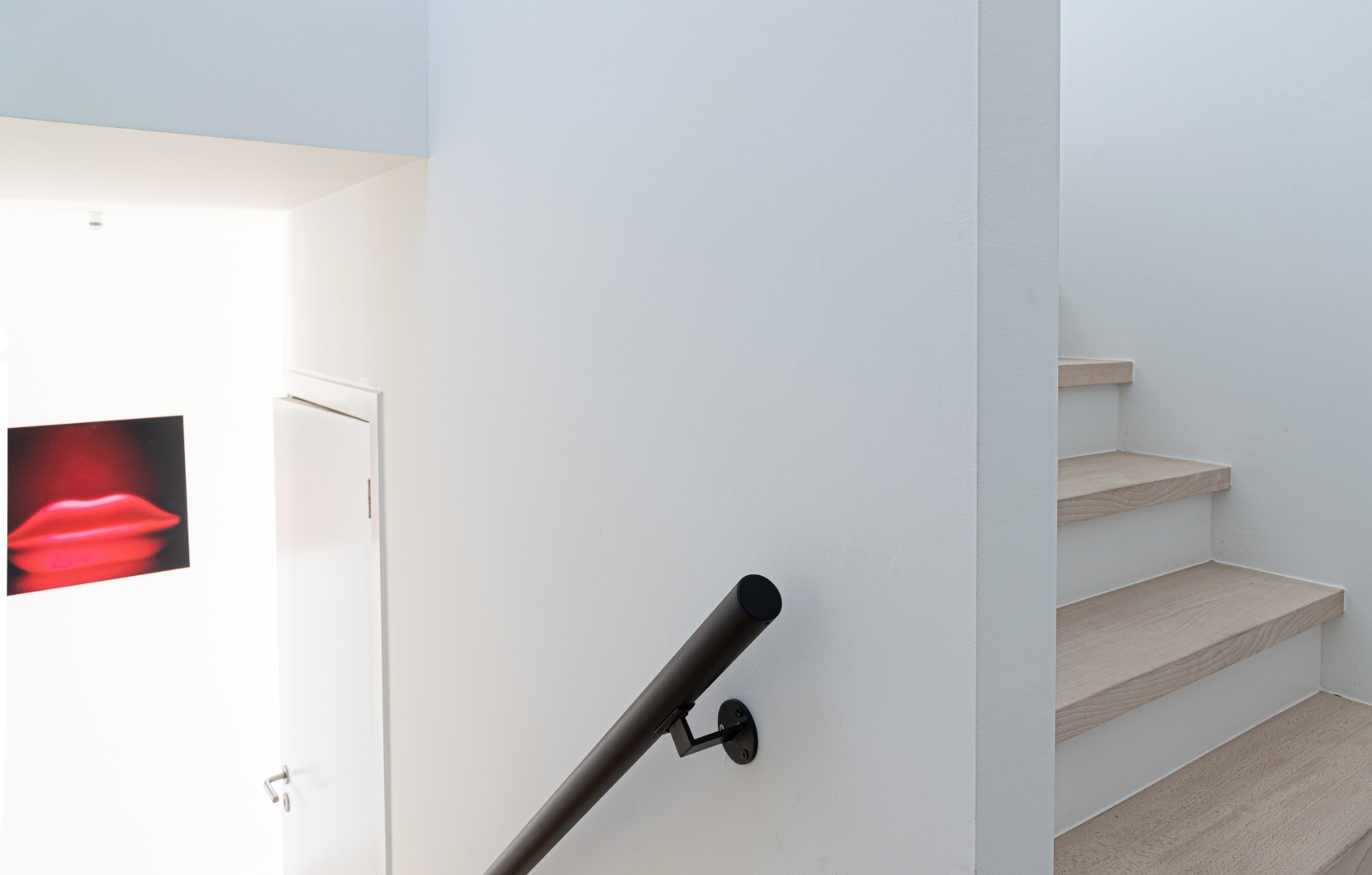 Houten trap met zwarte handleider aan witte muur
