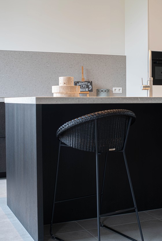 Zwart keukeneiland met rotan barkruk en stenen werkblad