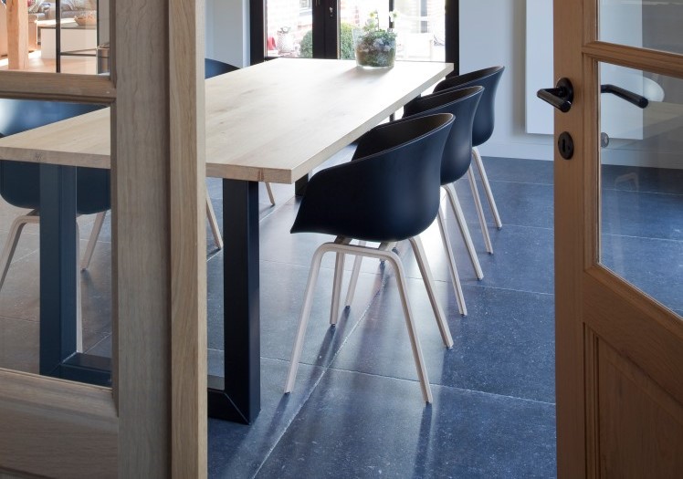 Houten eettafel met zwarte kuipstoelen op blauwe natuurstenen vloer