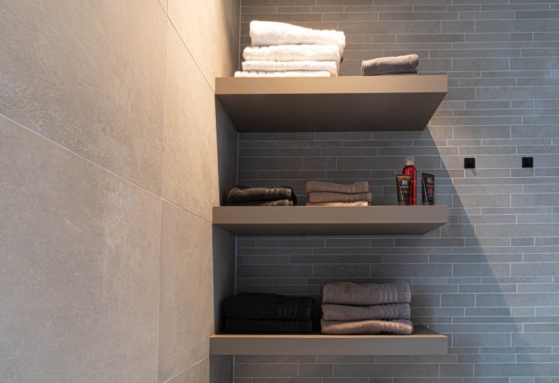Badkamer met zwevende planken en handdoeken op grijze tegelwand
