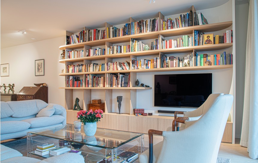 Woonkamer met houten wandkast vol boeken en blauwe zetel