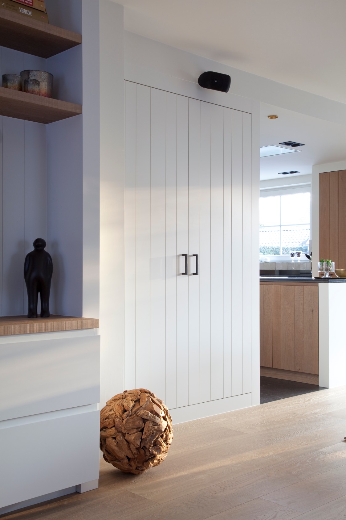 Witte inbouwkast met houten vloer en doorkijk naar keuken