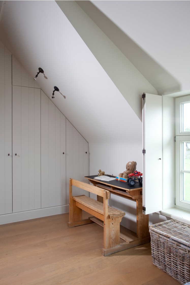 Zolderkamer met witte inbouwkasten en houten schoolbank