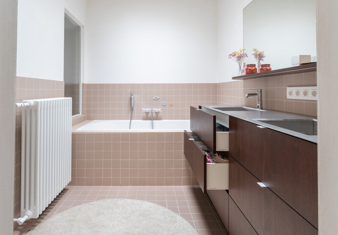 Badkamer met roze tegels bad en donkerhouten wastafelmeubel