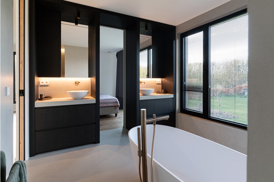 Badkamer met zwarte wastafelmeubels en doorkijk naar slaapkamer