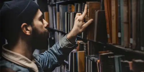 A young man browses through a row of books in a library.
