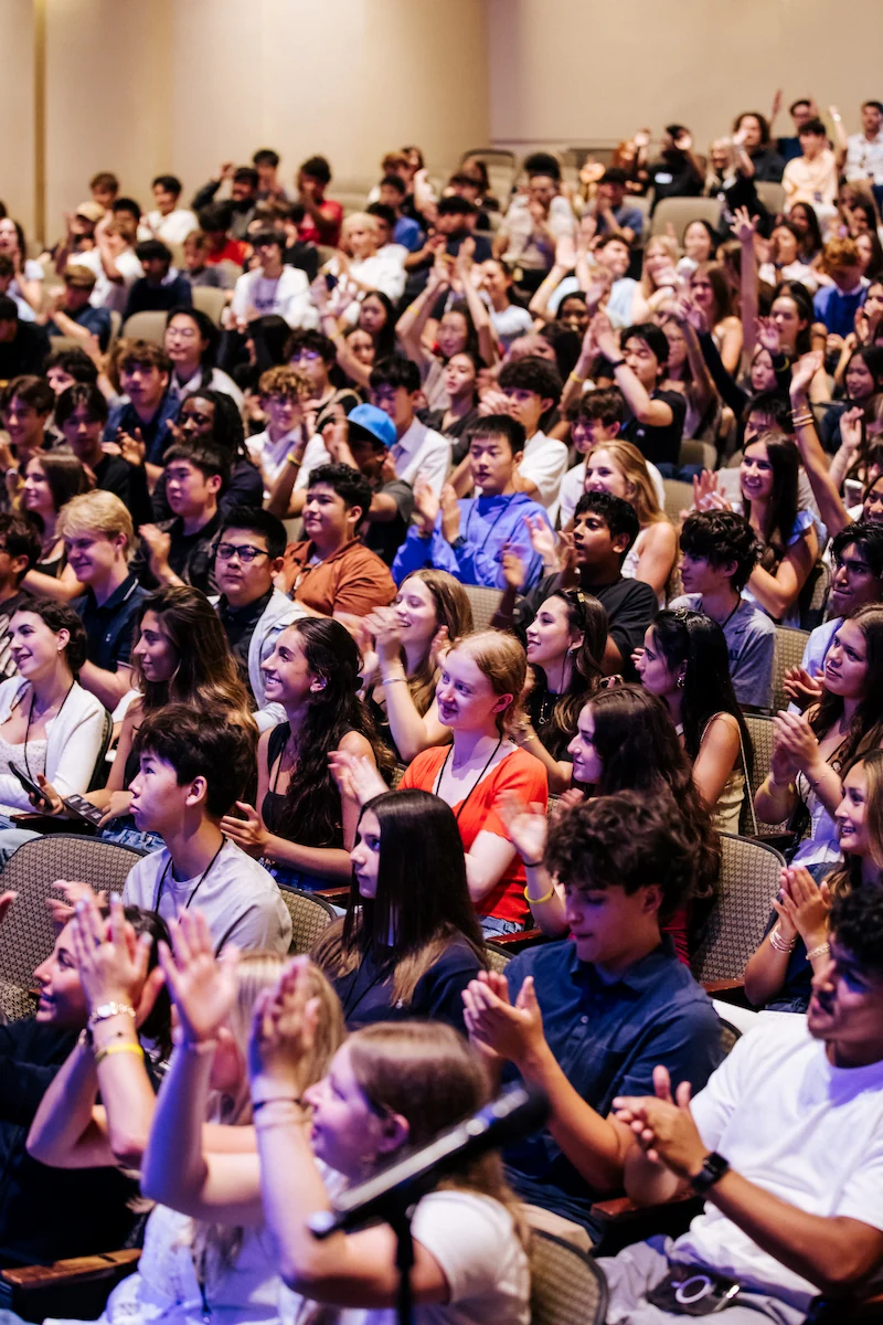 Audience of diverse young people sitting in an auditorium clapping and engaged.
