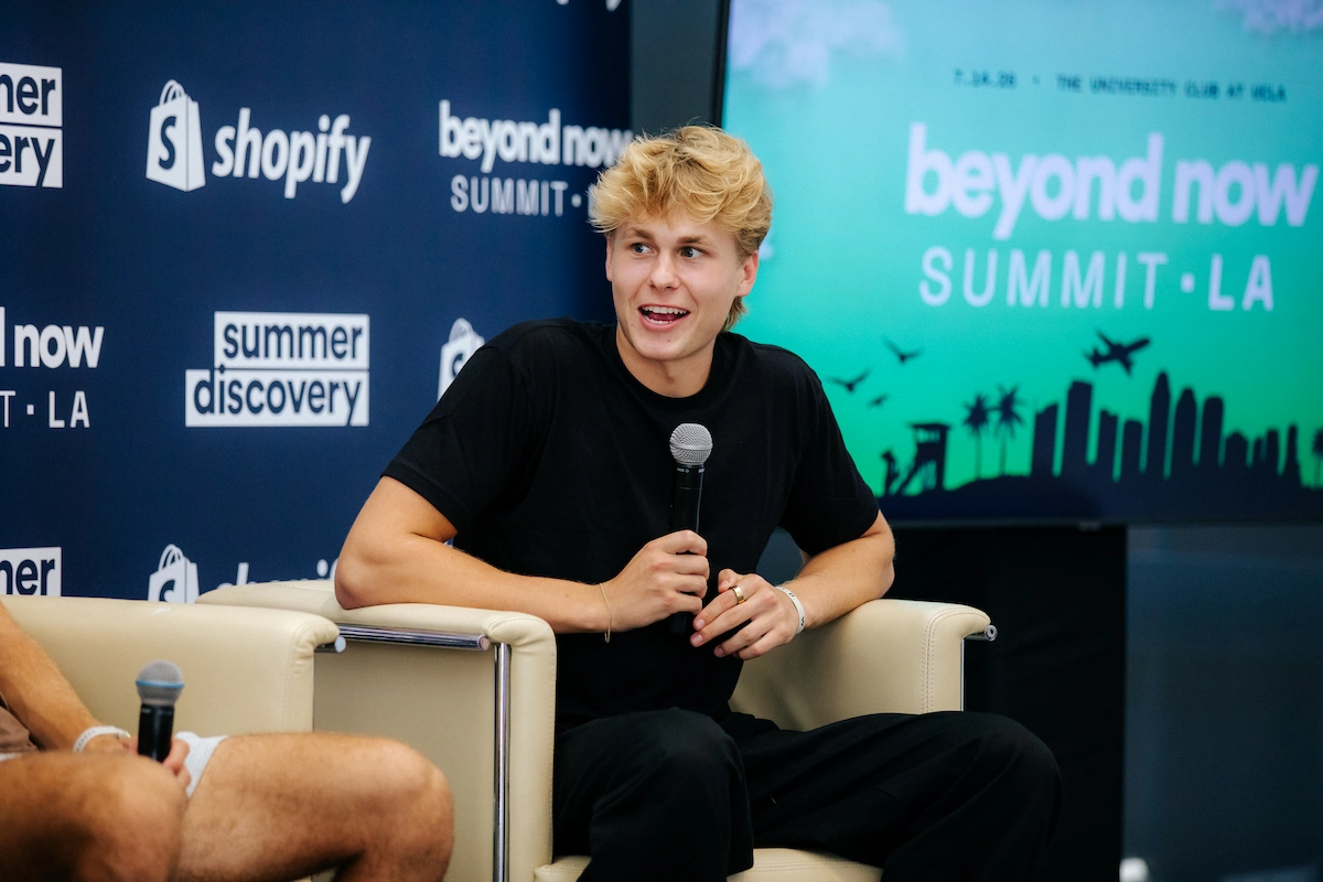 Young man with blond hair holding a microphone while seated during the Beyond Now Summit LA event.